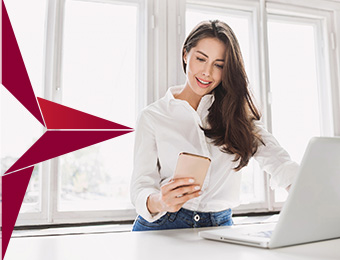 a woman standing in front of an open laptop while also looking at her phone